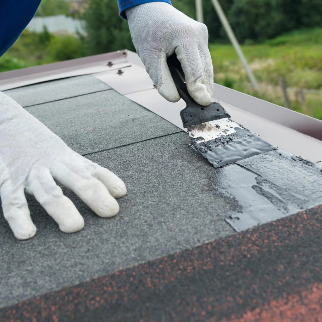 best roof sealant for asphalt shingles man wearing gloves and blue work suit applying a sealer to roof seams while installing shingles